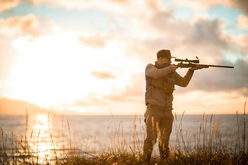 Chasseur visant avec une carabine à lunette au coucher du soleil près d’un lac au Canada.